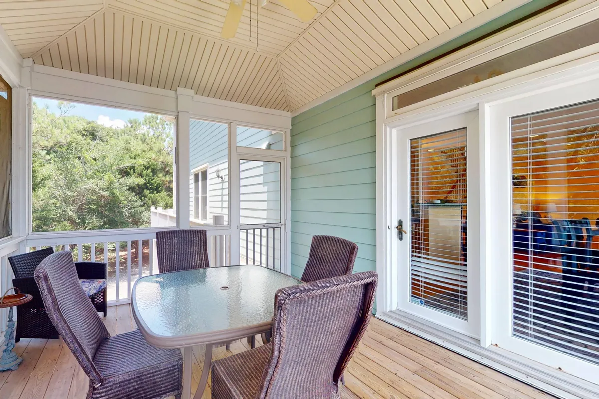 A sunlit interior dining area with a glass table, wicker chairs, and expansive windows offering inviting views. The space blurs the line between inside and outside, ideal for entertaining guests or enjoying meals with natural light pouring in.