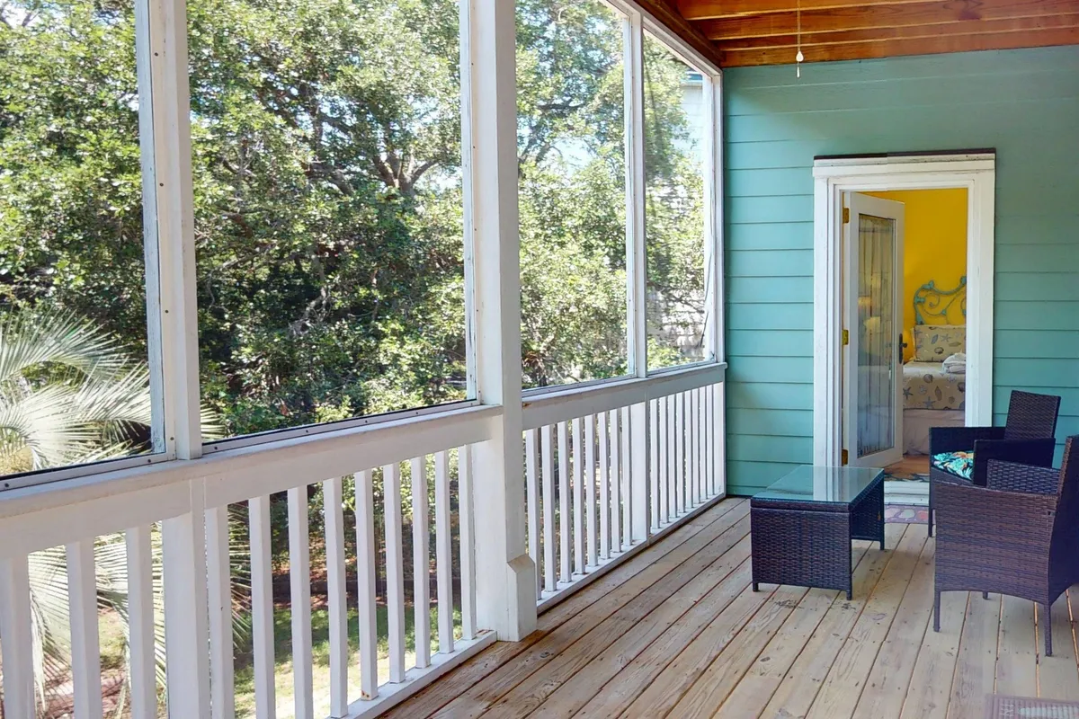 An exterior view of a screened porch with outdoor furniture, looking out onto abundant greenery. The porch is spacious, with comfortable seating ideal for wildlife viewing or simply enjoying the outdoors. The scene evokes relaxation and a strong sense of connection to the environment.
