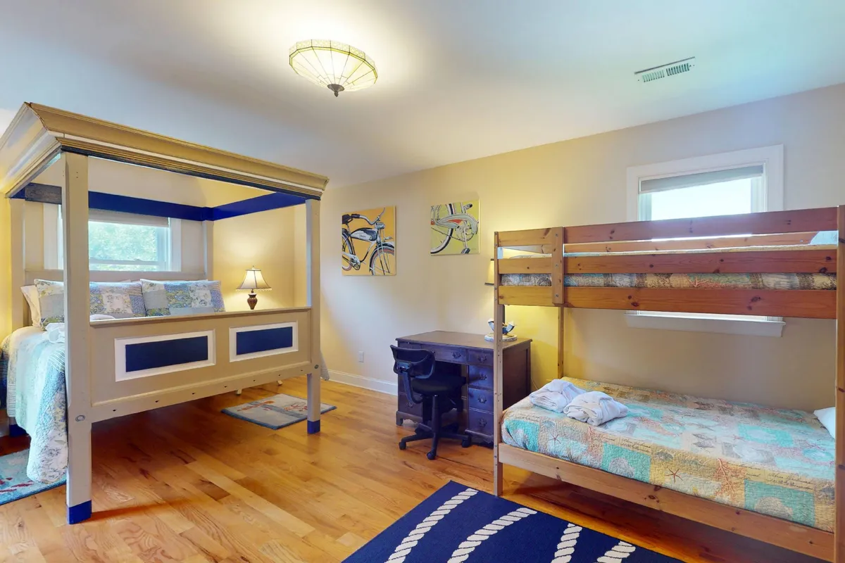 A family-friendly bedroom featuring both a canopy bed and a bunk bed, with a desk and playful wall art. The setup provides versatility for families and groups, catering to both kids and adults.