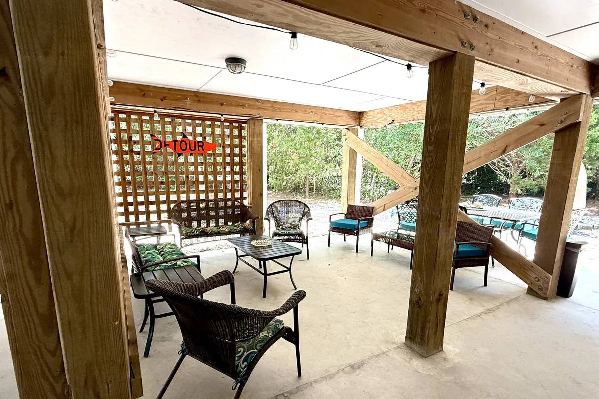 A cozy outdoor lounge setup on the deck, featuring woven chairs, a coffee table, and a lattice wall with string lights, all contributing to an atmosphere perfect for evening relaxation or casual socializing.