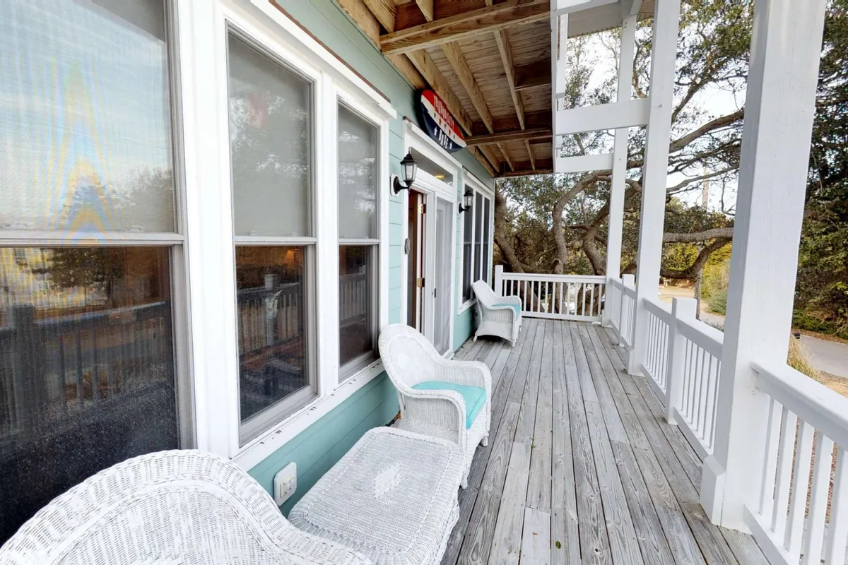 A tranquil wooden deck featuring wicker chairs, railings, and large windows. The setup is ideal for socializing, relaxing, or enjoying a meal outdoors, perfectly suited for group gatherings or casual al fresco dining.