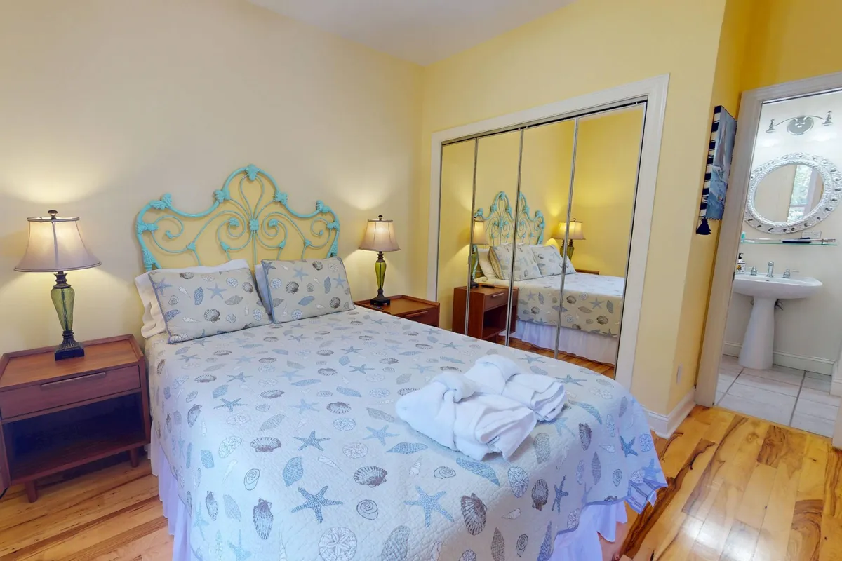 A tranquil bedroom with a decorative headboard, mirrored wardrobe, and nightstands with lamps. The room exudes a peaceful ambiance and is bathed in natural light, ideal for deep rest and relaxation.