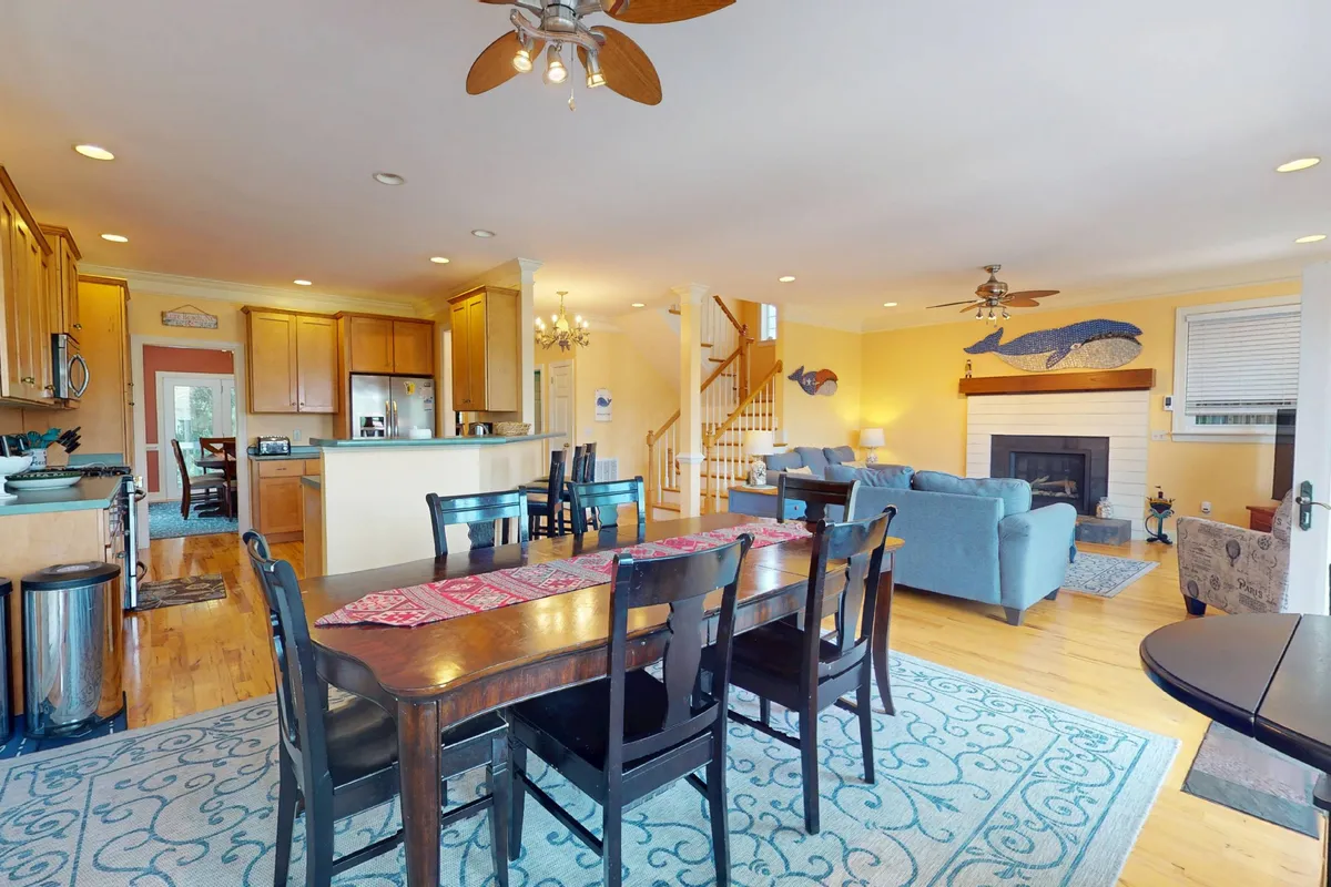 A spacious dining area with a large table, decorative rug, living area with fireplace, and staircase. The setting is ideal for family meals, celebrations, and social gatherings, exuding warmth and togetherness.