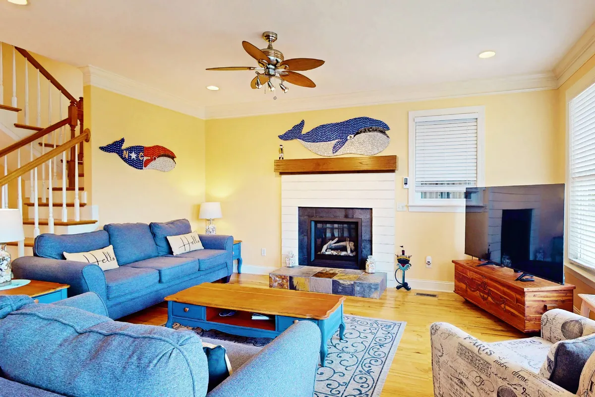 The living room features an inviting sofa set, a cozy fireplace, decorative wall art, a coffee table, and a television. The arrangement encourages family relaxation, movie nights, and cheerful gatherings.