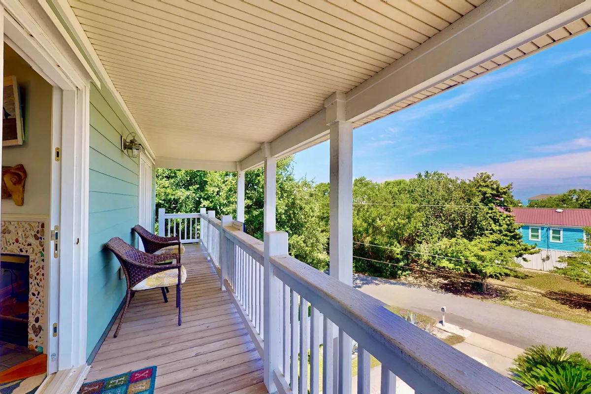 An inviting wooden deck with woven chairs set against lush green foliage and distant houses. The space offers a tranquil atmosphere, perfect for enjoying a quiet morning coffee, reading, or relaxing with friends while taking in serene views.