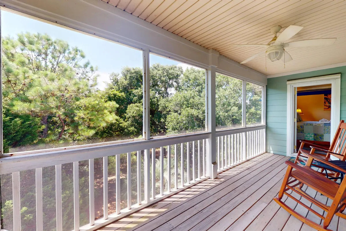 A tranquil exterior porch scene featuring rocking chairs on a screened porch overlooking lush greenery. The ambiance is peaceful, inviting guests to relax, read a book, or sip their morning coffee while feeling immersed in nature. The open view to the outside emphasizes the seamless indoor-outdoor connection.
