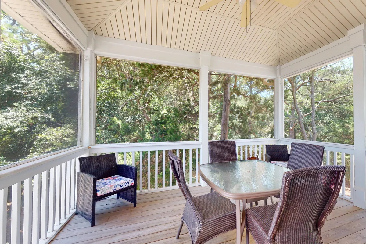 A bright, screened-in interior dining area with a glass table and woven chairs atop wooden flooring. The airy feel and views to the outside suggest a space that's protected but visually connected to the natural environment, making it perfect for group breakfasts or evening meals in comfort.